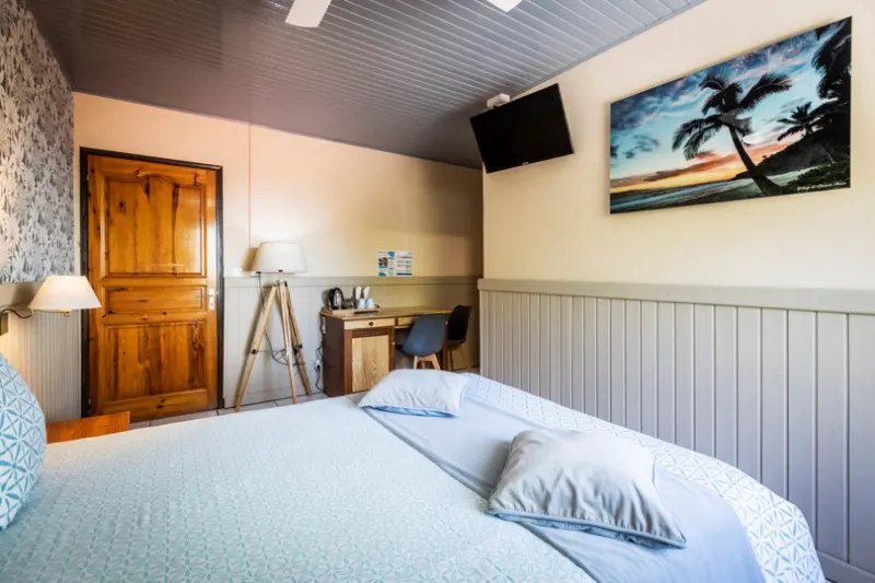 Une chambre claire avec un grand lit, un bureau en bois et une photo de plage au mur