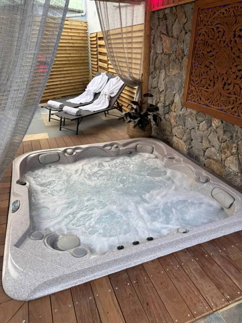 Le spa extérieur en bois et pierre, avec deux transats et des peignoirs